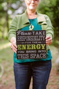 Patti holds a sign in front of her that reads: "Please take responsibility for the energy you bring into this space."