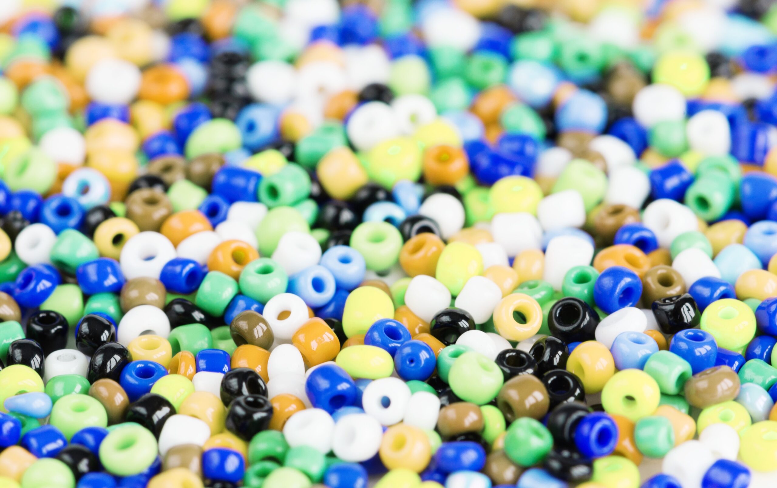 photo of multi-colored beads for needlework are scattered on a white background